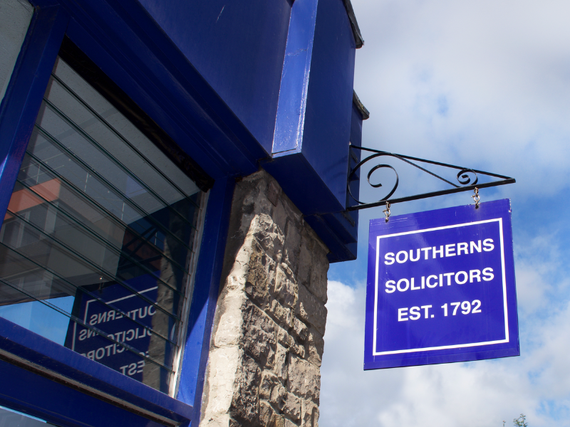 Image of Exterior of the building with a swinging sign with the Southerns Solicitors logo on and blue sky with clouds in the background.